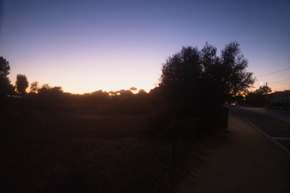 the sun is setting in the distance behind a fence