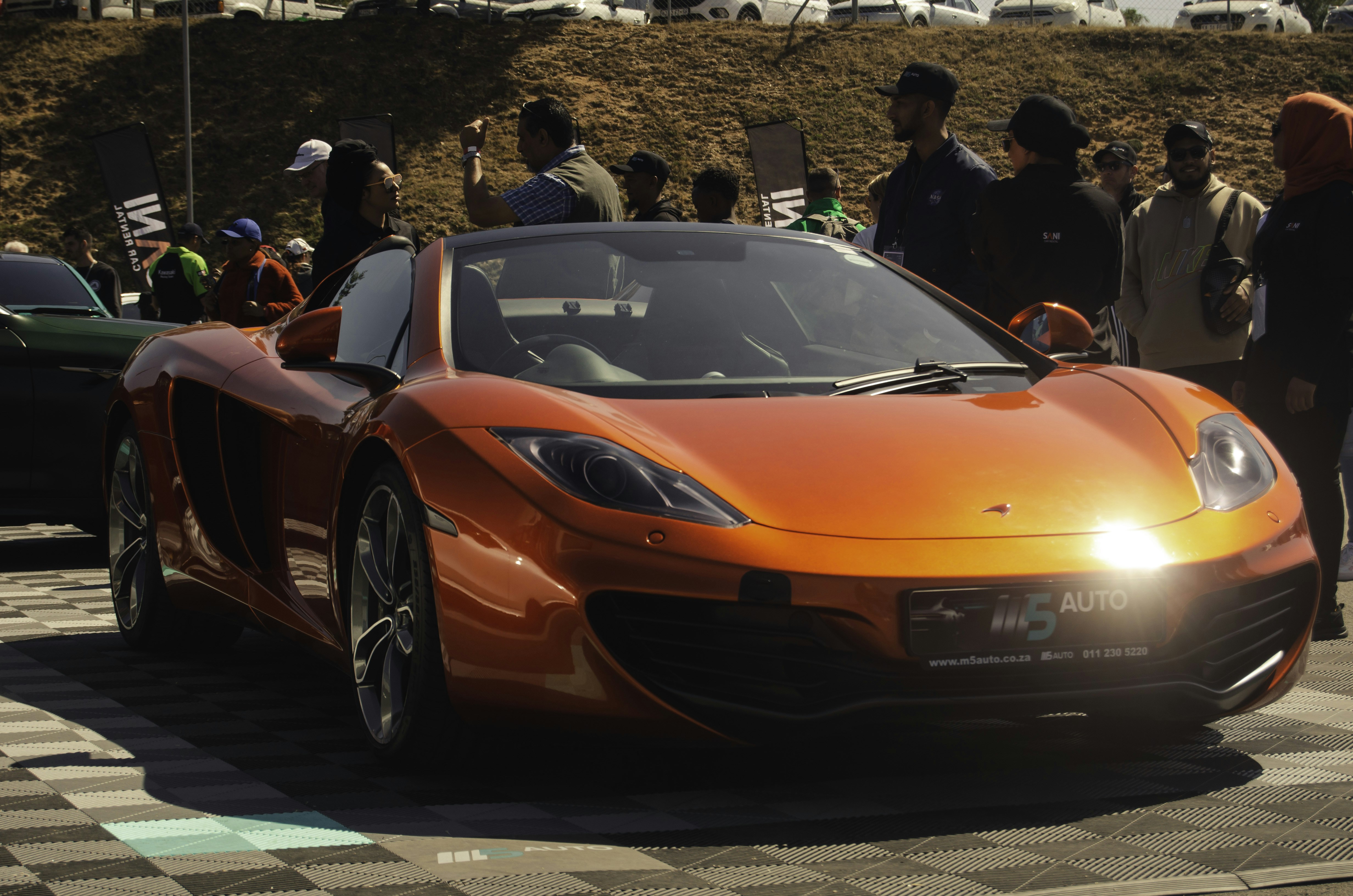 Sebuah mobil sport oranye diparkir di depan kerumunan orang