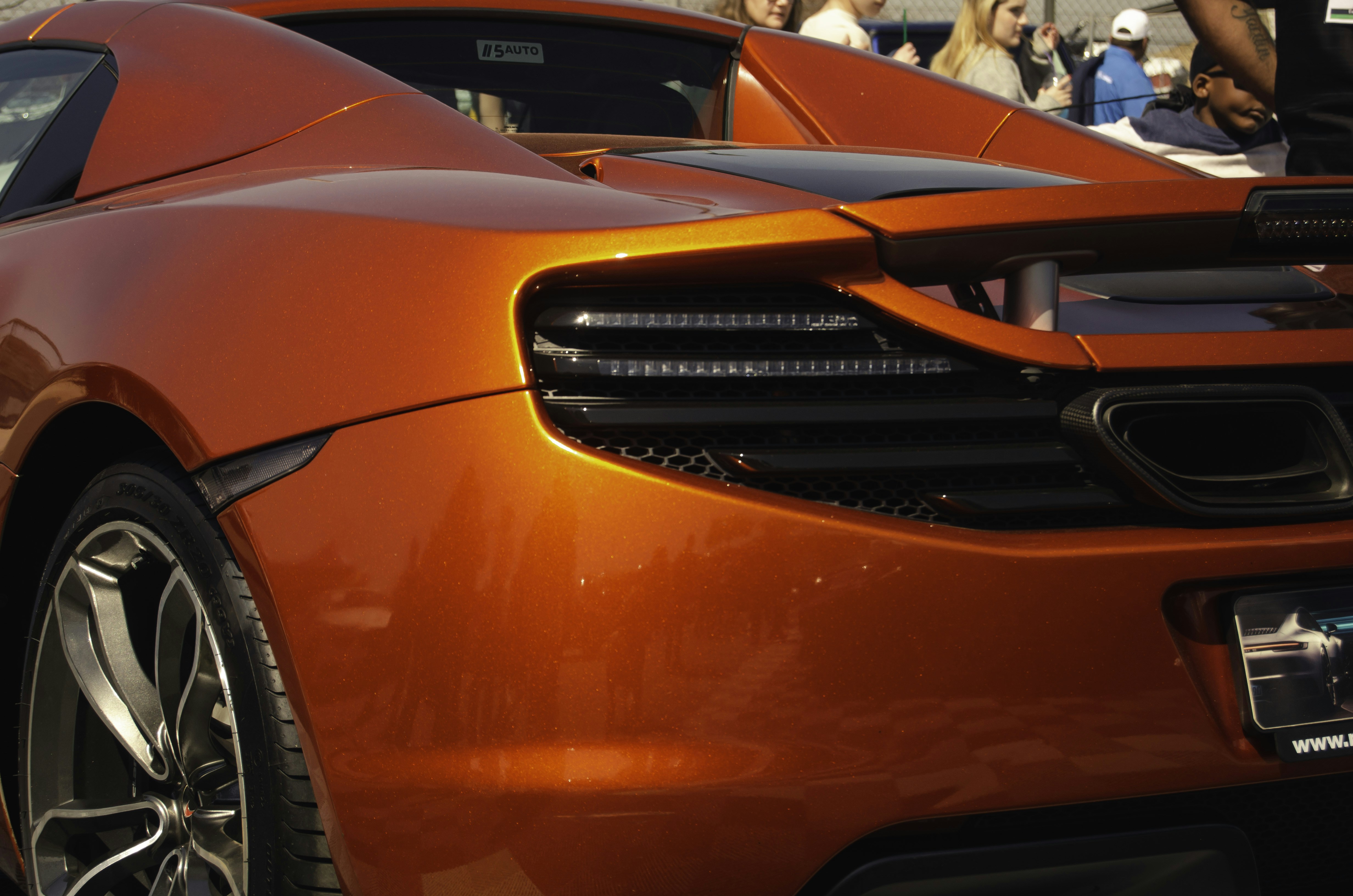 Sebuah mobil sport oranye diparkir di depan kerumunan orang