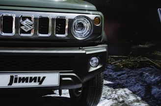 Close-up of a vehicle's front portion featuring a detailed view of the grille, headlights, and bumper. The logo, a prominent S, is clearly visible in the center of the grille. The setting appears to be outdoors with rocks and vegetation faintly visible in the background.