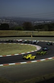 Wide shot of a racetrack with multiple cars taking a sharp turn during a race.