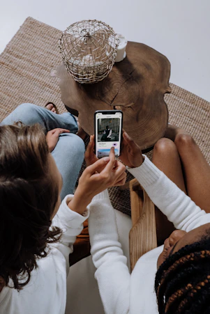 two women sitting on a couch looking at a cell phone