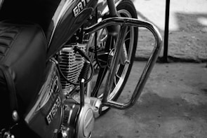 A close-up view of a motorcycle, focusing on the engine and part of the frame. The bike features chrome details, a seat with a stitched pattern, and visible branding on the fuel tank.