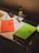 A dimly lit desk contains an assortment of study materials. An orange notebook titled 'Urban Edge' is placed next to a green notebook with a sketched face. Several pens, an eraser, and a ruler are scattered across the surface. A pencil case and a bottle with a black lid labeled 'Frozen' are also present.