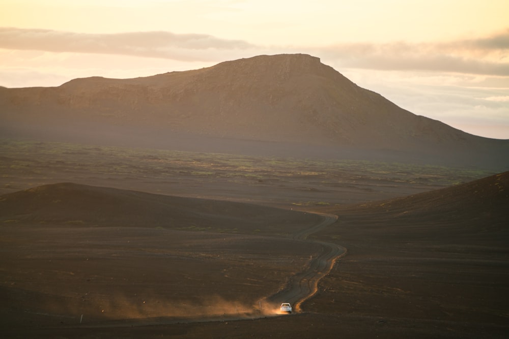 a car driving down a dirt road near a mountain