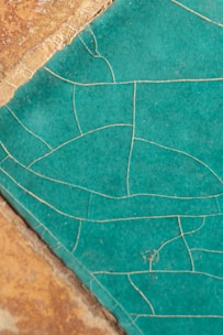 An intricate pattern on a blue-green ceramic surface with visible cracks and lines, alongside a section of a rough, brown textured material.