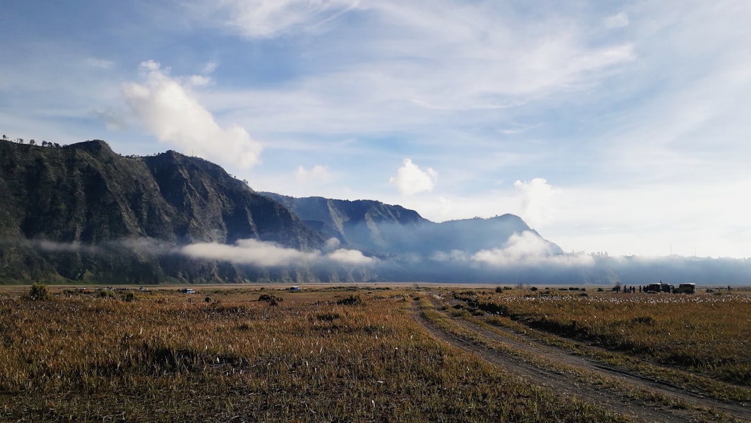 a dirt road in front of a mountain range, Misty Morning at Mount Bromo
