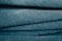 A close-up view of stacked, folded blue towels showing their soft, textured surface. The light catches the fibers, giving the fabric a slightly shiny look.