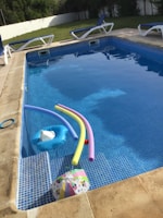 A sparkling clean backyard pool with teal-colored tile accents and purple pool toys floating.
