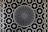 A patterned metal grate features a circular design in the center with radiating slots and a surrounding intricate geometric grid. The grid consists of repeating circular and square shapes connected by intersecting lines.