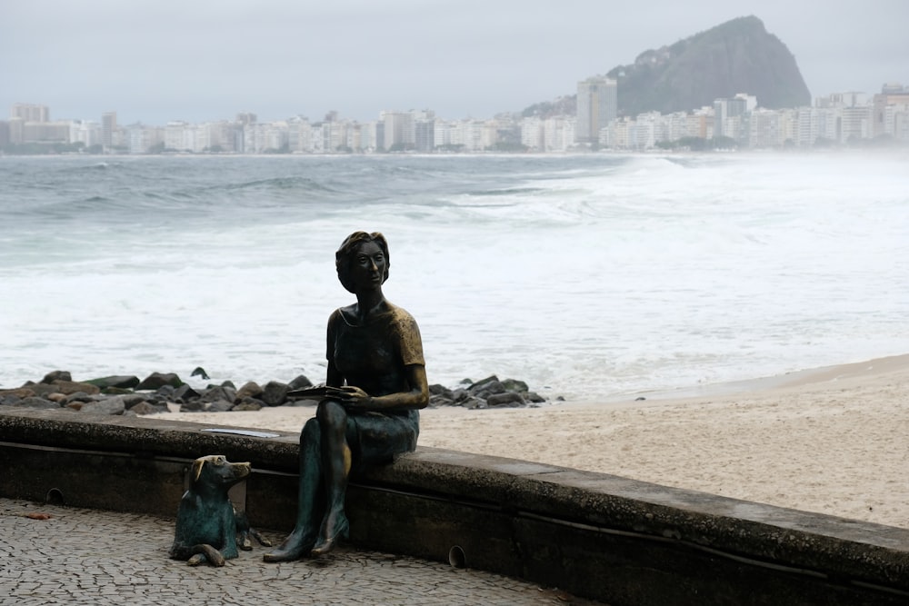 a statue of a woman sitting on a wall next to the ocean