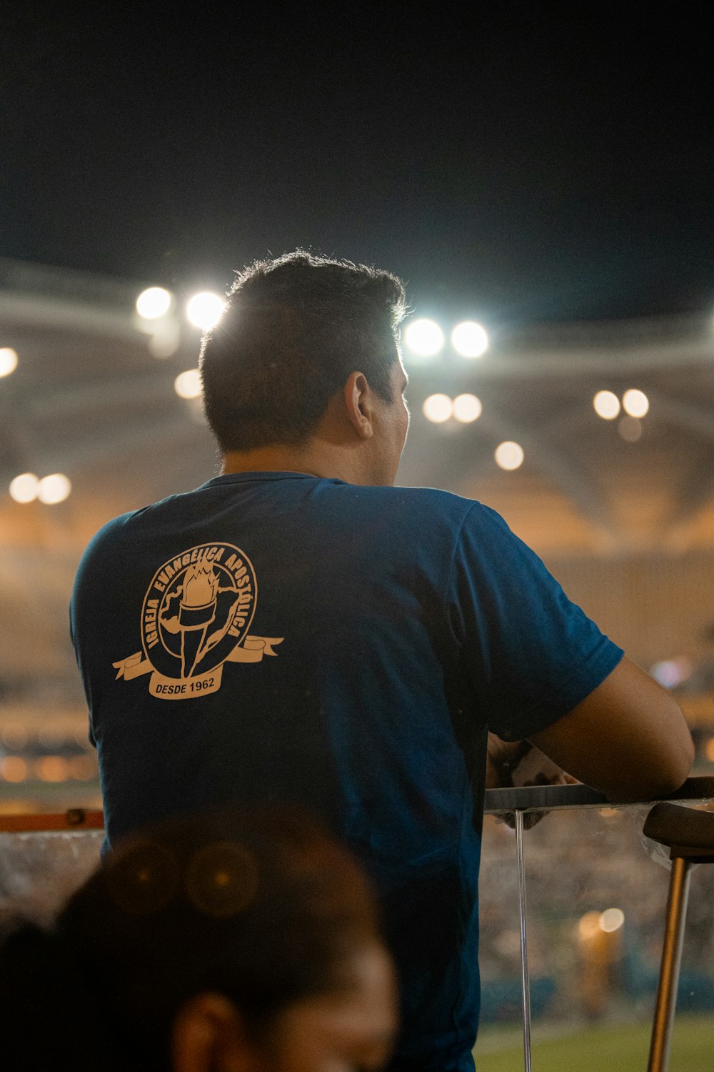a man in a blue shirt is sitting in a stadium