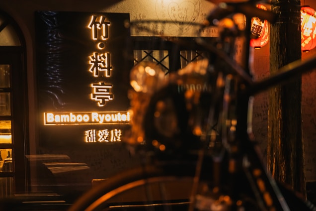 A cozy Japanese inn warmly lit at dusk welcoming travelers, with a subtle Indonesian flag detail beside the entrance.