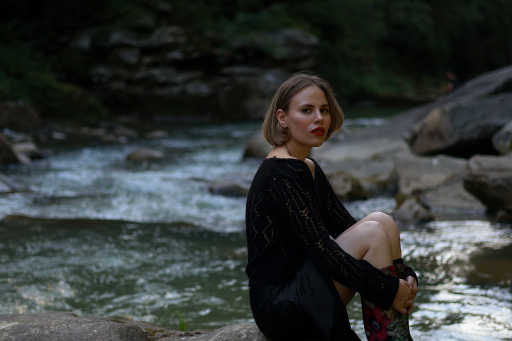 a woman sitting on a rock next to a river