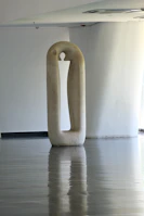 A sleek modern sculpture displayed in a sunlit gallery space.