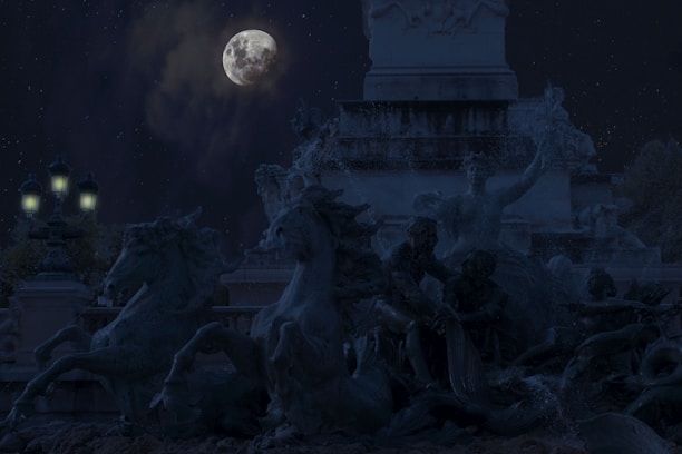 A moonlit scene featuring a dramatic sculpture of expressive horses and human figures. The focus is on the detailed forms of the statues against a dark night sky, with the full moon and stars adding a mystical element. Street lamps glow softly nearby, enhancing the ambiance.