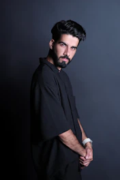 A sleek editorial shot of a male model wearing contemporary fashion accessories against a soft beige studio backdrop.