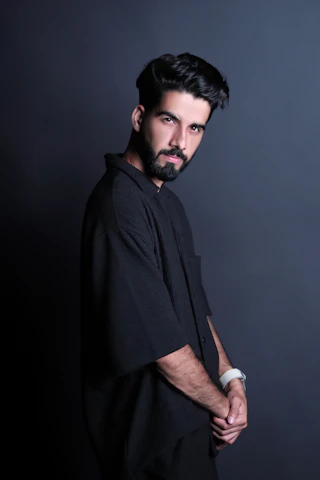 A sleek editorial shot of a male model wearing contemporary fashion accessories against a soft beige studio backdrop.