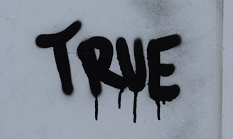 the word true is spray painted on a white wall