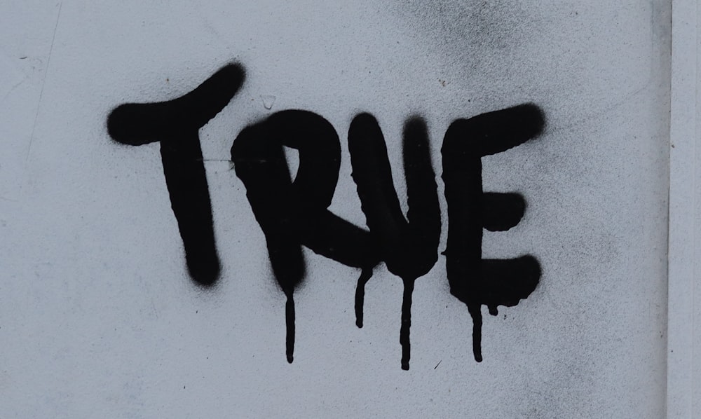 the word true is spray painted on a white wall