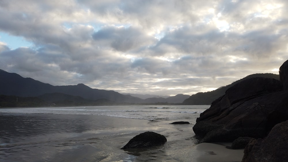 a beach with rocks and water under a cloudy sky