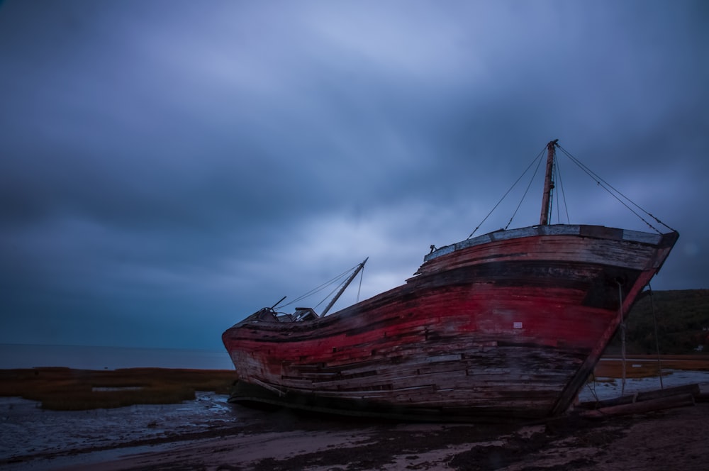 a boat sitting on top of a beach under a cloudy sky