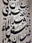 Large black Arabic script covers a white wall, featuring bold calligraphic letters with a variety of shapes and diacritical marks. The text is arranged in a visually dynamic and artistic manner, creating an intricate pattern.