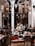 A cozy indoor setting with a group of musicians playing traditional instruments. The performers are dressed in cultural attire and are surrounded by an intimate audience seated at tables. Several ornate hanging lamps add a warm ambiance to the room, which features arches and wooden accents.