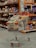 A shopping cart filled with a variety of packaged goods, including snacks and household items, is situated in an aisle of a grocery store. The shelves in the background are stocked with various colorful products.