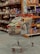 A shopping cart filled with a variety of packaged goods, including snacks and household items, is situated in an aisle of a grocery store. The shelves in the background are stocked with various colorful products.