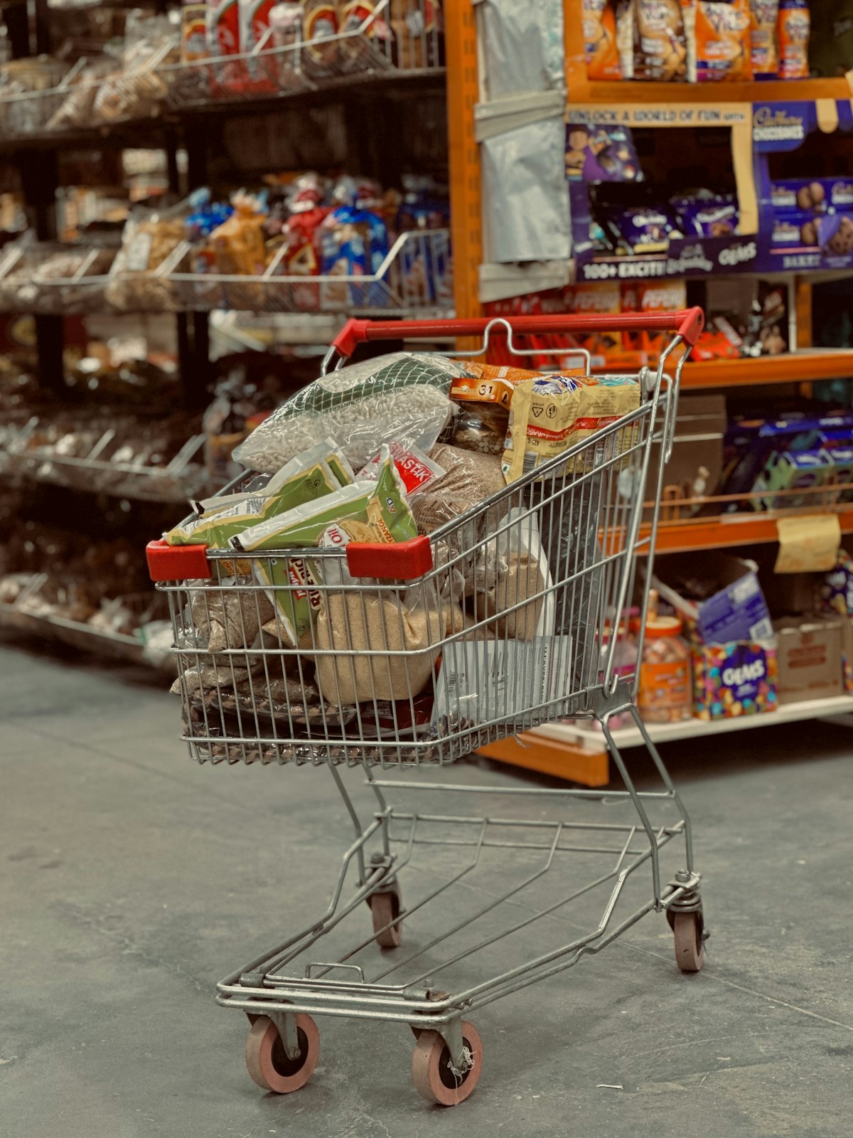 A shopping cart full of groceries in a store aisle representing the stockpiling trend among American consumers