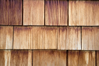 A pattern of evenly spaced, overlapping wooden shingles with visible grain texture and varying shades of brown.