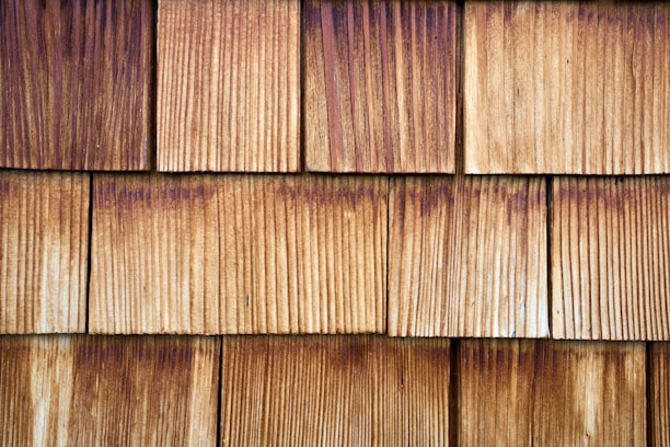 A pattern of evenly spaced, overlapping wooden shingles with visible grain texture and varying shades of brown.