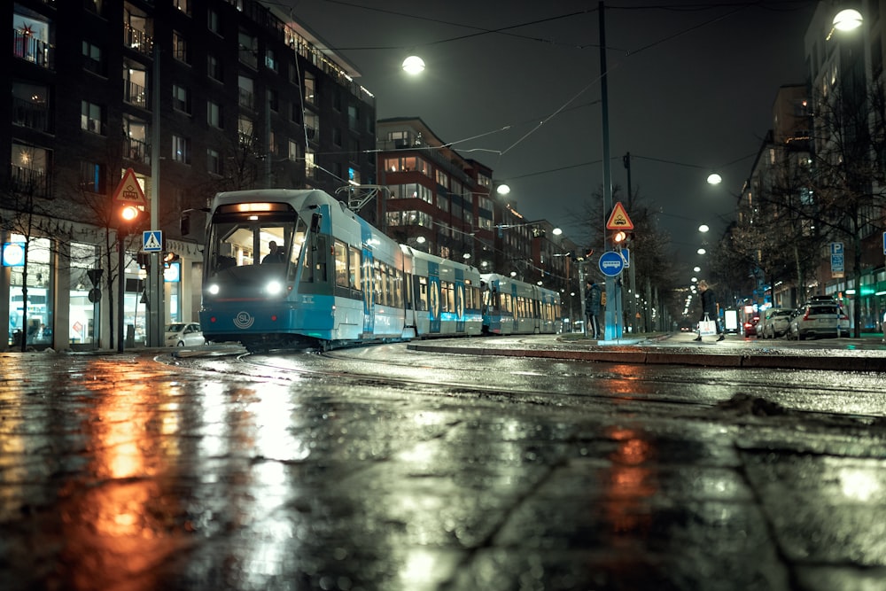 a blue and white train on a city street at night