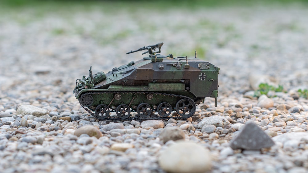 a toy army tank sitting on top of a gravel field