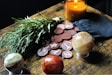 A table arrangement featuring a bundle of herbs, a lit amber candle, a black pouch, round wooden tokens with runic symbols, and three decorative gemstone spheres.