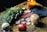 A table arrangement featuring a bundle of herbs, a lit amber candle, a black pouch, round wooden tokens with runic symbols, and three decorative gemstone spheres.