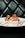 Two pieces of sushi are elegantly arranged on a white plate, garnished with vibrant toppings like green herbs and red roe. The plate is artistically accented with lines of red sauce. The background is a tufted, dark leather surface, giving a sophisticated ambiance.