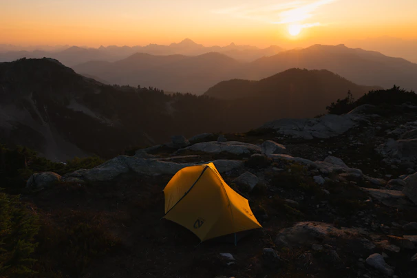 Camp setup with cozy tents nestled among rocky terrain at dusk.