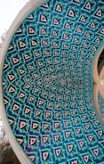 An intricately designed dome with a repeating geometric pattern featuring blue and turquoise hues. The design incorporates symmetrical shapes enclosed within a circular structure, hinting at Middle Eastern or Islamic architectural influences.