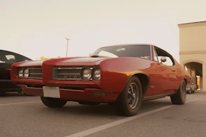 Model wearing a red muscle car tee standing beside a classic Dodge Charger.