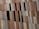 A close-up view of a building facade covered with vertical panels in shades of beige, brown, and grey. Some panels are replaced by black rectangular windows, creating a pattern. The panels appear to be slightly angled, adding to the visual interest.