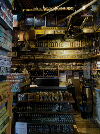 A cozy corner of the barrosviva store showcasing a variety of colorful beverage bottles neatly arranged on wooden shelves.