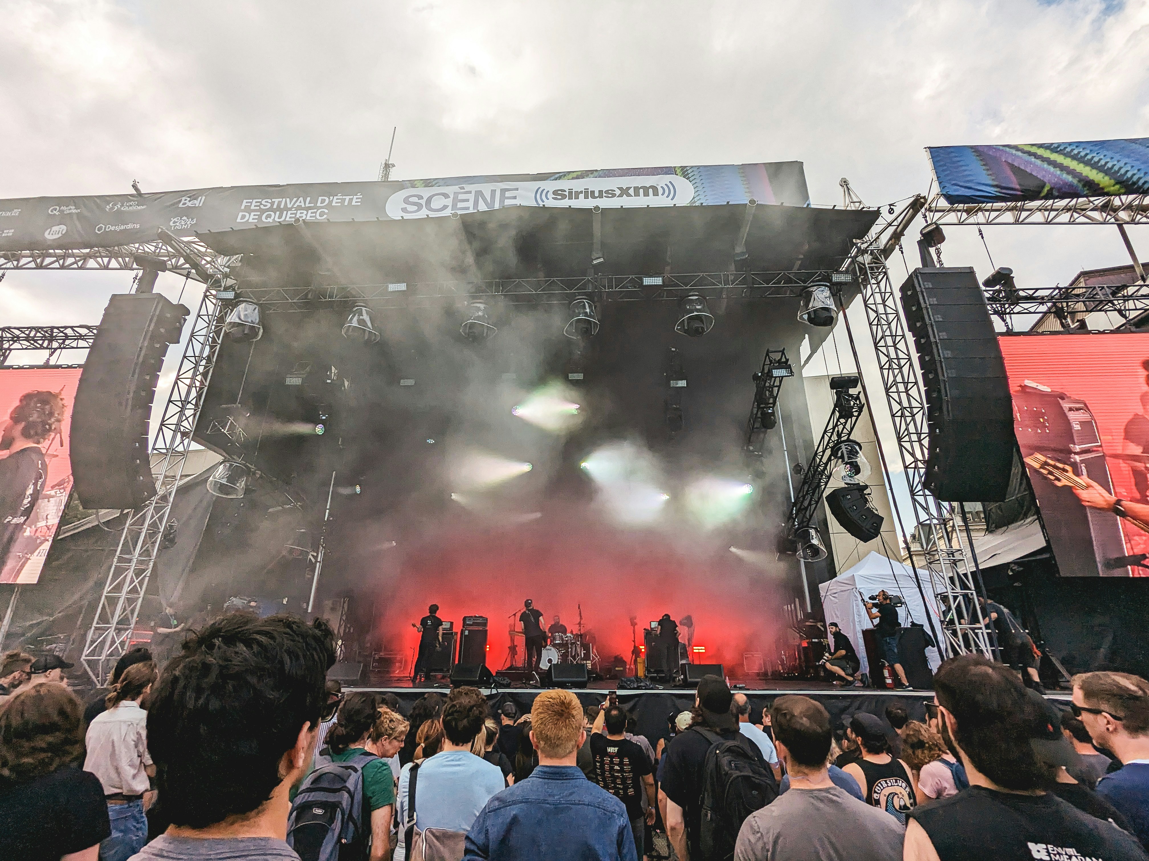 Live band performance on stage with dramatic backlit smoke and red stage lighting, crowd in foreground