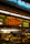 A food stall or counter with signage advertising 'Beef & Cheddar Croissant' and 'Italian Sausage'. The interior is dimly lit with hanging pendant lights. There's a food preparation area visible through the glass, containing kitchen equipment and a roll of paper towels.