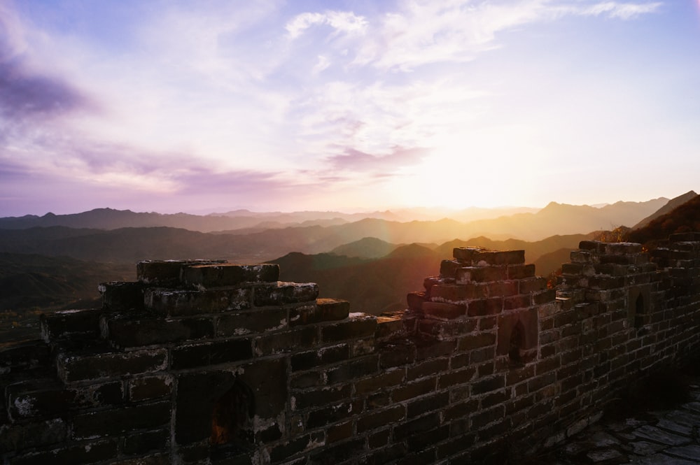 the sun is setting over the mountains behind a wall