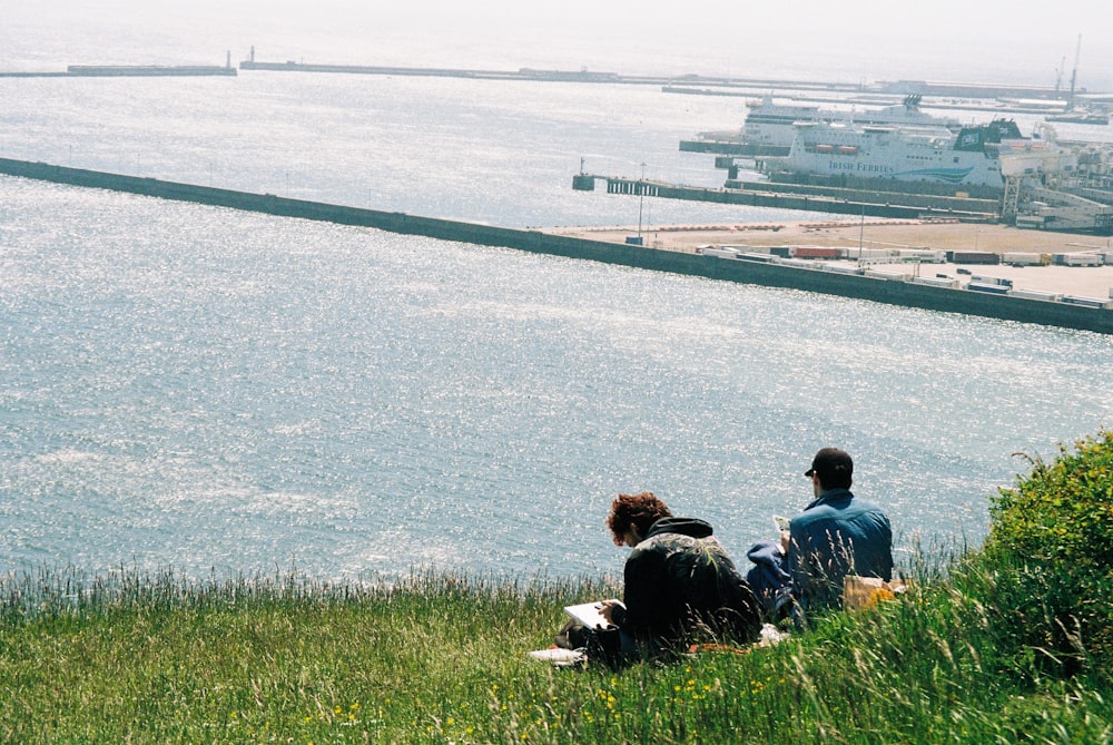 three people sitting on a hill overlooking a body of water