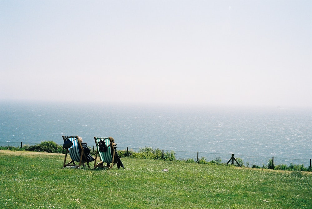 a couple of lawn chairs sitting on top of a lush green hillside