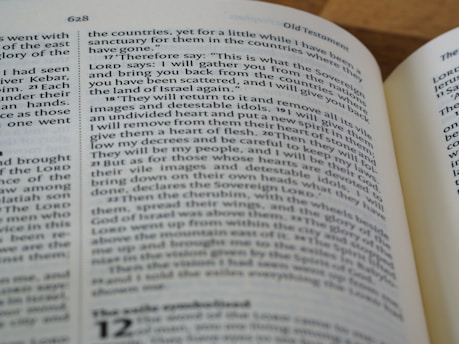 A close-up view of an open book displaying text from a religious scripture. The text is in black font on white pages. The page heading 'Old Testament' is visible and the verses appear to be discussing themes of gathering and restoration.
