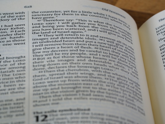 A close-up view of an open book displaying text from a religious scripture. The text is in black font on white pages. The page heading 'Old Testament' is visible and the verses appear to be discussing themes of gathering and restoration.